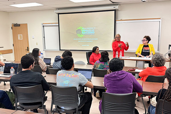 three women speak in a classroom